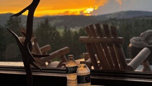 A sunset view from a window with a lamp, two water bottles, and wooden chairs. - Charming 3 bedroom Log cabin with WiFi in Kalispell (Kalispell)