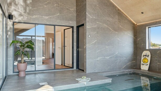 A modern indoor pool area with a clear view of the outside through glass doors, a potted plant, and a motivational sign by the pool. - 5 Star Holiday Home in Henne (Henne)