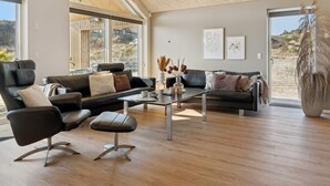 A modern living room with a leather sofa, a coffee table, and a large window overlooking a natural landscape. - 5 Star Holiday Home in Henne (Henne)