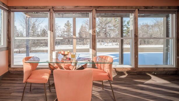 Un coin repas avec une table en verre, des chaises de couleur pêche et une vue sur un paysage enneigé, visible à travers de grandes fenêtres.