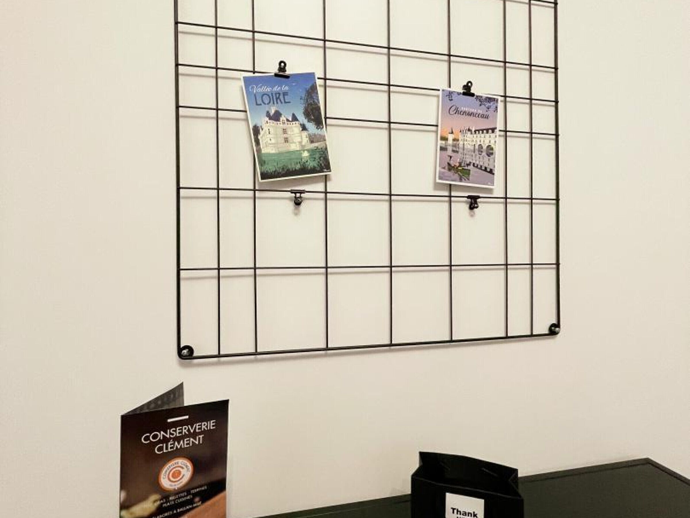 A bulletin board with two postcards pinned on it, and a brochure on a table.