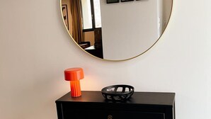 A black console table with a round mirror above it, a small orange object, and a black basket. - Luxury cottage with heated pool and SPA in the heart of the Loire Valley (Ballan-Miré)