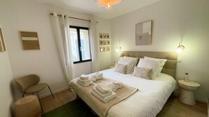A neatly arranged bedroom with a bed, a chair, a bedside table, and a window with curtains. - Luxury cottage with heated pool and SPA in the heart of the Loire Valley (Ballan-Miré)