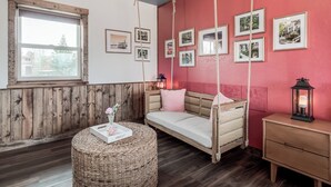 Una habitación acogedora con piso de madera, una cama con mecedora, un reposapiés de mimbre y una mesita de noche con un farol.