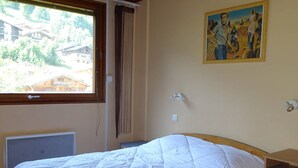 Une chambre à coucher avec un lit, une fenêtre avec des rideaux, un radiateur, une lampe fixée au mur et un tableau.