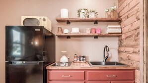 A compact kitchen with a black refrigerator, wooden shelves, and pink cabinets.