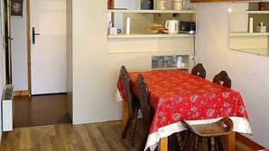 Una zona de menjador amb una taula i cadires de fusta, un mantell vermell i una cuina amb prestatges a la part superior.