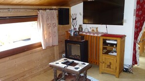 A cozy room with a wooden ceiling, a television mounted on the wall, a small table with a cowhide rug, and a wooden cabinet with a red cloth on top.