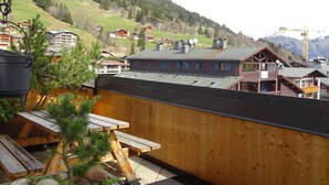 A wooden deck with picnic tables overlooking a mountainous village with traditional houses and a ski lift in the background.