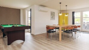 A modern living room with a pool table, a dining area with a wooden table and chairs, and a bright yellow door. - 4 Star Holiday Home in Vaeggerlose (Vaeggerlose)