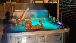 A hot tub with two people relaxing, surrounded by a brick wall and a wooden fence. - 4 Star Holiday Home in Vaeggerlose (Vaeggerlose)