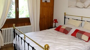 A bedroom with a wooden floor, a bed with a gold frame, white bedding, and a window with curtains. - 4-bedroom apartment for 8 with garage, near shops and cable cars (Les Gets)