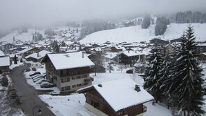 A snow-covered village with traditional wooden houses, a main road, and a mountain in the background. - 4-bedroom apartment for 8 with garage, near shops and cable cars (Les Gets)