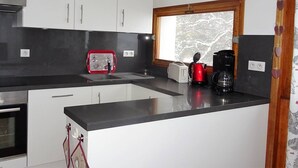A modern kitchen with white cabinets, a black countertop, a red toaster, a coffee maker, and a window with a view of trees. - 4-bedroom apartment for 8 with garage, near shops and cable cars (Les Gets)