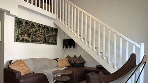 A living room with a brown sofa, a round coffee table, a hammock chair, a staircase with white railings, and a large abstract painting on the wall.