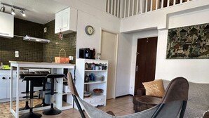 A modern kitchen with a dining area, a hammock chair, and a living room with a couch and a painting.