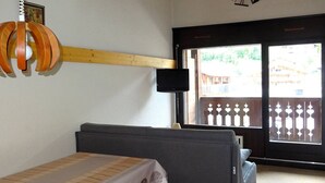 A room with a bed, a wooden shelf, a television, and a view of the outside. - Spacious Studio Duplex in Les Gets - Sleeps 6, Garage, Near Slopes and Shops (Les Gets)