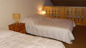 A bedroom with two beds, a wooden nightstand, and a wall-mounted lamp. - Spacious Studio Duplex in Les Gets - Sleeps 6, Garage, Near Slopes and Shops (Les Gets)