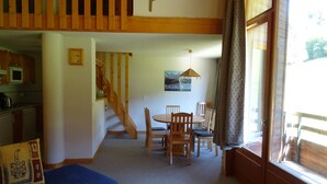 A cozy living room with a blue sofa, a dining table with chairs, a staircase, and a kitchen area.