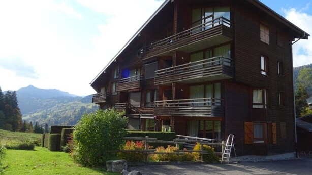 A multi-story wooden building with balconies, set against a mountainous backdrop.