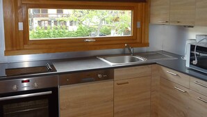Ett kök med träskåp, en inbyggd diskmaskin, en diskho och ett fönster med utsikt över ett bostadsområde.