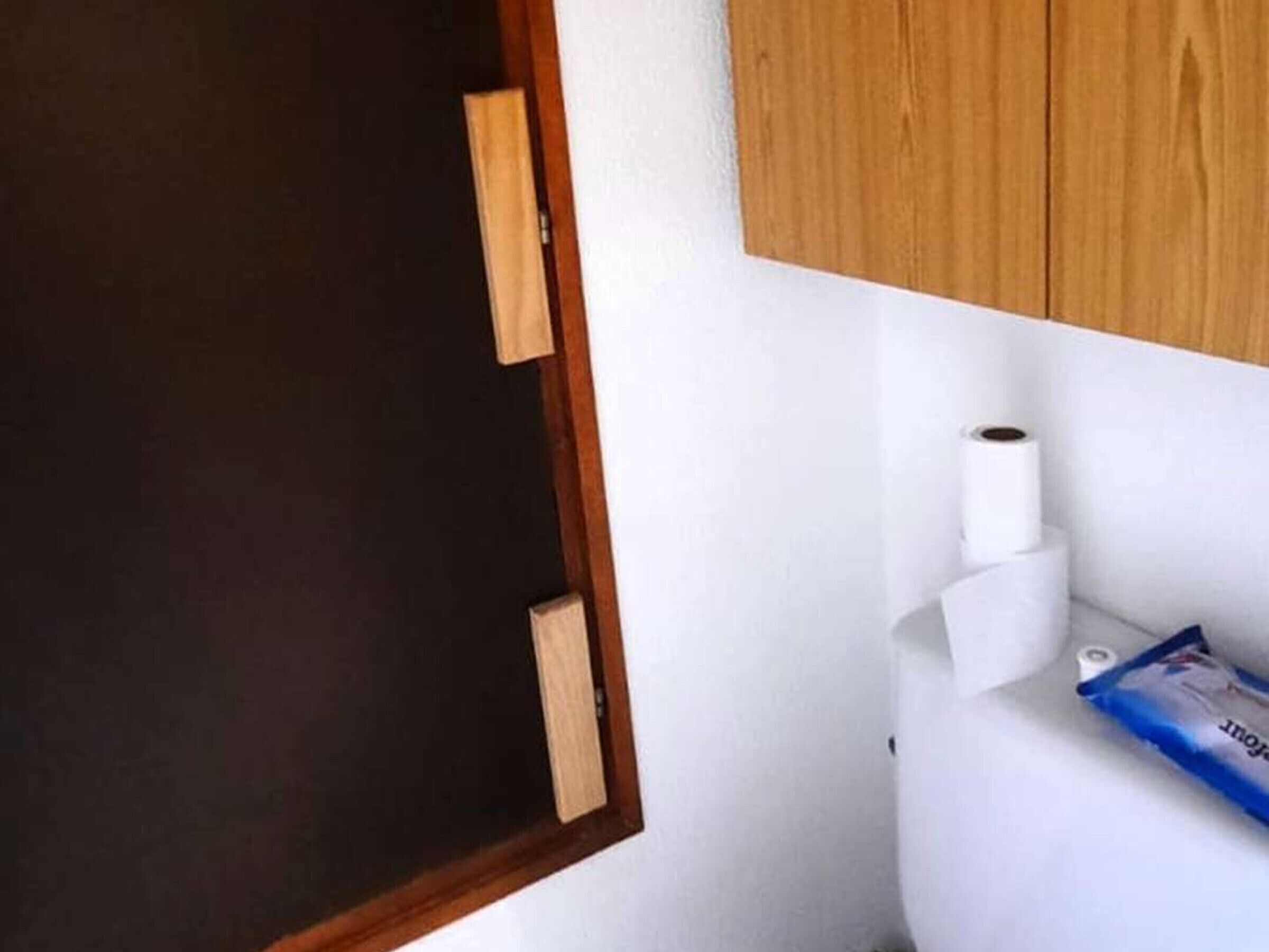 Un baño con puerta de madera, inodoro blanco y un paquete azul en el suelo.