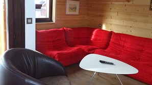 Une pièce chaleureuse avec un canapé rouge, un fauteuil en cuir noir et une table basse blanche.