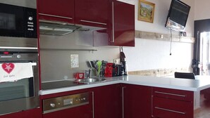 Une cuisine moderne avec des meubles de couleur rouge, des appareils en acier inoxydable et un téléviseur à écran plat fixé au mur.