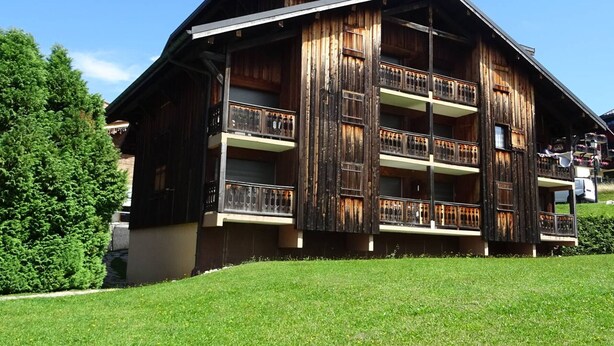 Un bâtiment en bois à plusieurs étages, doté de balcons, vraisemblablement un hôtel ou une maison d’hôtes, entouré de verdure.