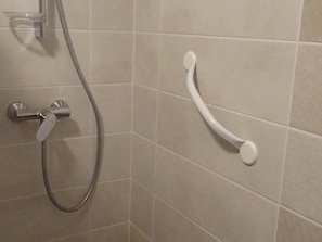Un espace douche équipé d’un pommeau de douche à main et d’une barre d’appui fixée au mur.