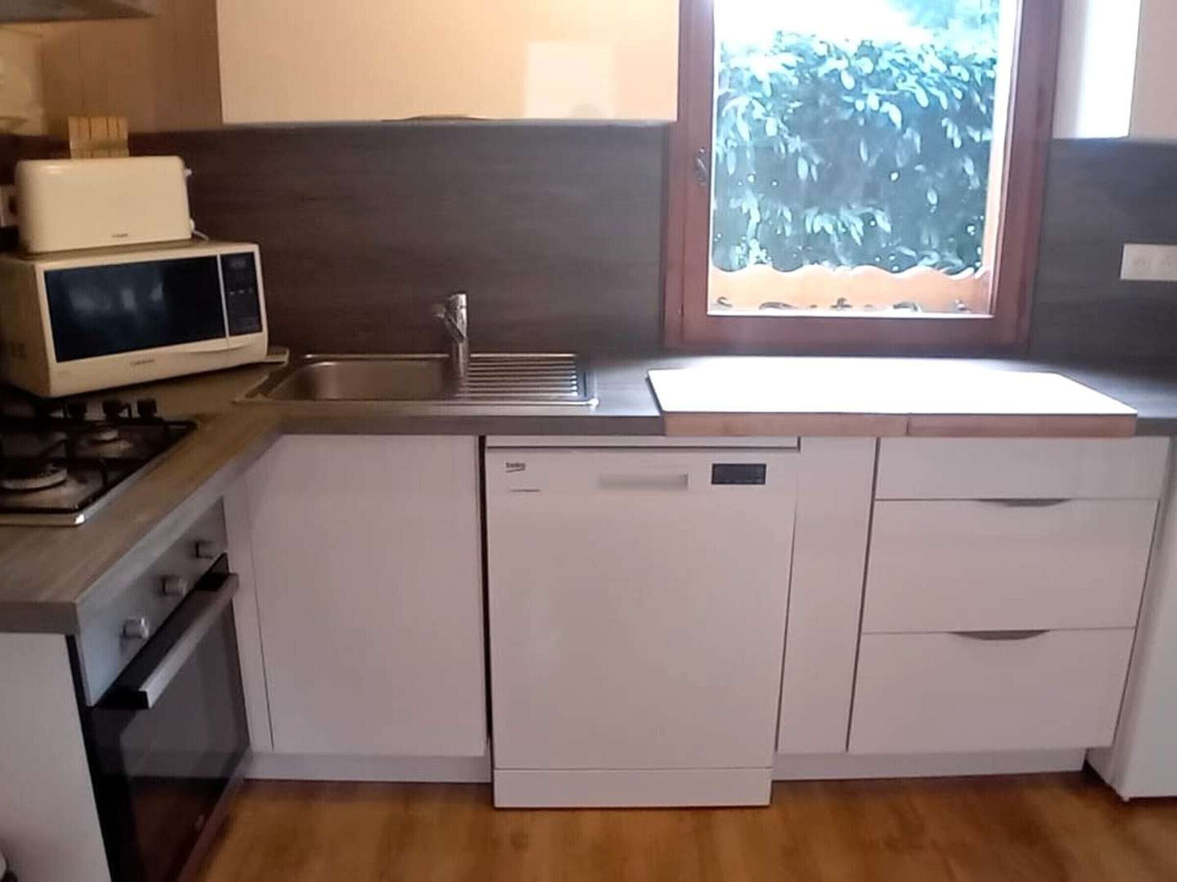 Een kleine keuken met een magnetron, spoelbak en vaatwasser.