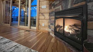 Un intérieur chaleureux avec une cheminée en pierre, un plancher en bois et une porte vitrée donnant sur un espace extérieur.