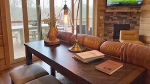 Un salon chaleureux avec un canapé en cuir, une table basse en bois ornée d’un vase et de livres, une lampe de table et un téléviseur fixé au mur.