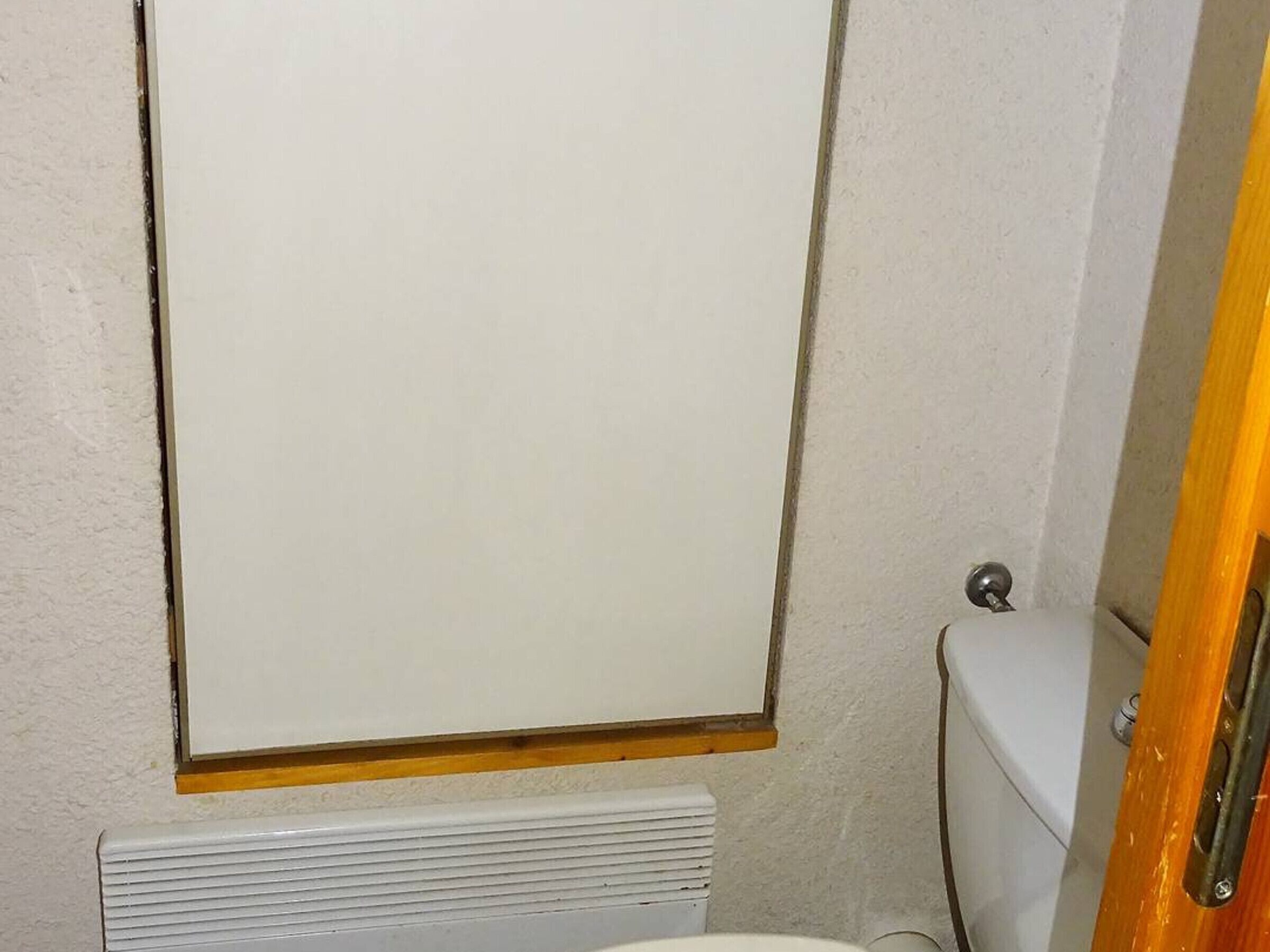 Un baño con inodoro, un radiador blanco y un espejo con marco de madera.