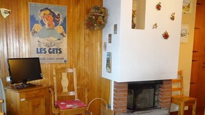 A cozy living room with a fireplace, wooden furniture, and a poster on the wall. - Les Gets: Bright 2-room duplex, ski-in/out, 250m from center, for 6/8 people (Les Gets)