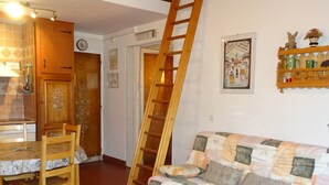 A cozy living room with a wooden ladder, a patterned sofa, and a dining area with a table and chairs. - Les Gets: Bright 2-room duplex, ski-in/out, 250m from center, for 6/8 people (Les Gets)