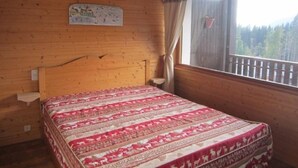 A wooden cabin room with a bed, a window with a view of trees, and a map on the wall. - Les Gets: Bright 2-room duplex, ski-in/out, 250m from center, for 6/8 people (Les Gets)