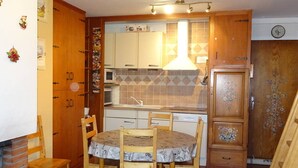 A compact kitchen with wooden cabinets, a microwave, and a sink. There is a dining table with chairs and a decorative door. - Les Gets: Bright 2-room duplex, ski-in/out, 250m from center, for 6/8 people (Les Gets)