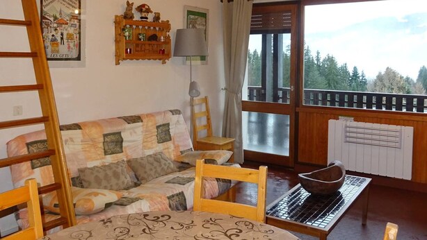 A cozy living room with a wooden sofa, a wooden table, and a view of a balcony with a railing. - Les Gets: Bright 2-room duplex, ski-in/out, 250m from center, for 6/8 people (Les Gets)