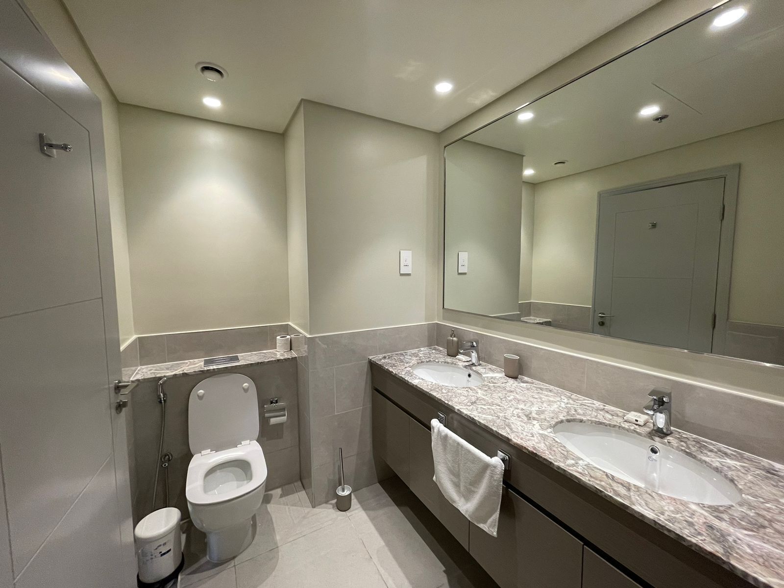 A modern bathroom with a toilet, bidet, and two sinks with marble countertops.