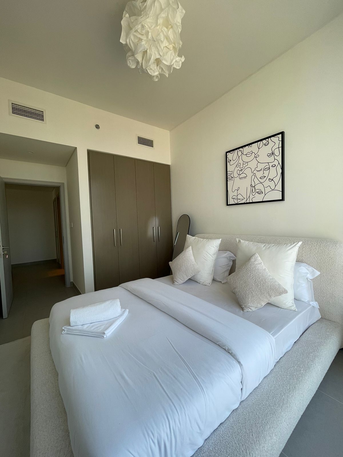 A modern hotel room with a large bed, a wardrobe, and a unique wall art piece.
