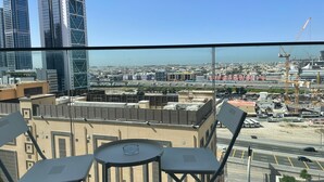 Vue depuis le balcon d’un immeuble de grande hauteur, avec une table et des chaises, donnant sur un paysage urbain composé de bâtiments modernes et de grues de construction.