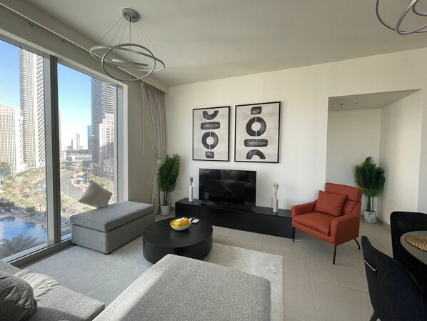 A modern living room with a large window, a flat-screen TV, a sofa, a red armchair, and two abstract paintings. - Two Bedroom Damac Majestine-StayOnHomes  (Dubai)