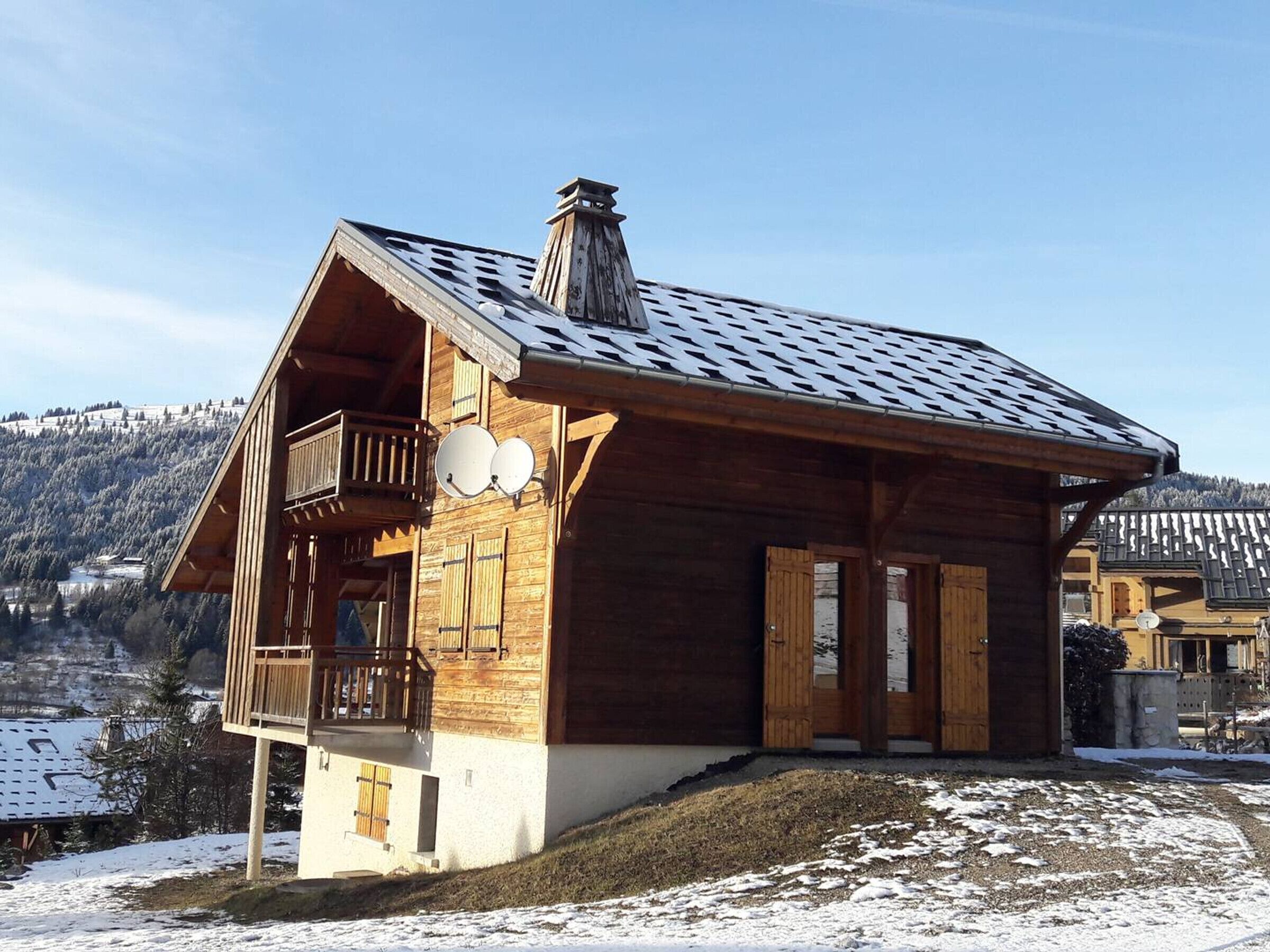 Un chalet de madera con balcón, antenas parabólicas y vistas a colinas nevadas.