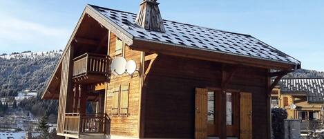 Un chalet de madera con balcón, antenas parabólicas y vistas a colinas nevadas.