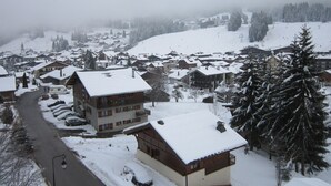 A snow-covered village with traditional chalet-style buildings, a winding road, and a prominent mountain in the background. - Studio in Les Gets - 4 people - Central, parking, quiet (Les Gets)