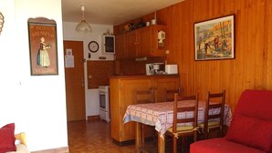 A cozy living room with a red sofa, a dining table with chairs, and a kitchen area with wooden cabinets and a stove. - Studio in Les Gets - 4 people - Central, parking, quiet (Les Gets)