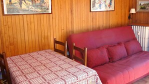 A room with wooden panel walls, a red sofa, a table with a checkered tablecloth, and two framed pictures. - Studio in Les Gets - 4 people - Central, parking, quiet (Les Gets)