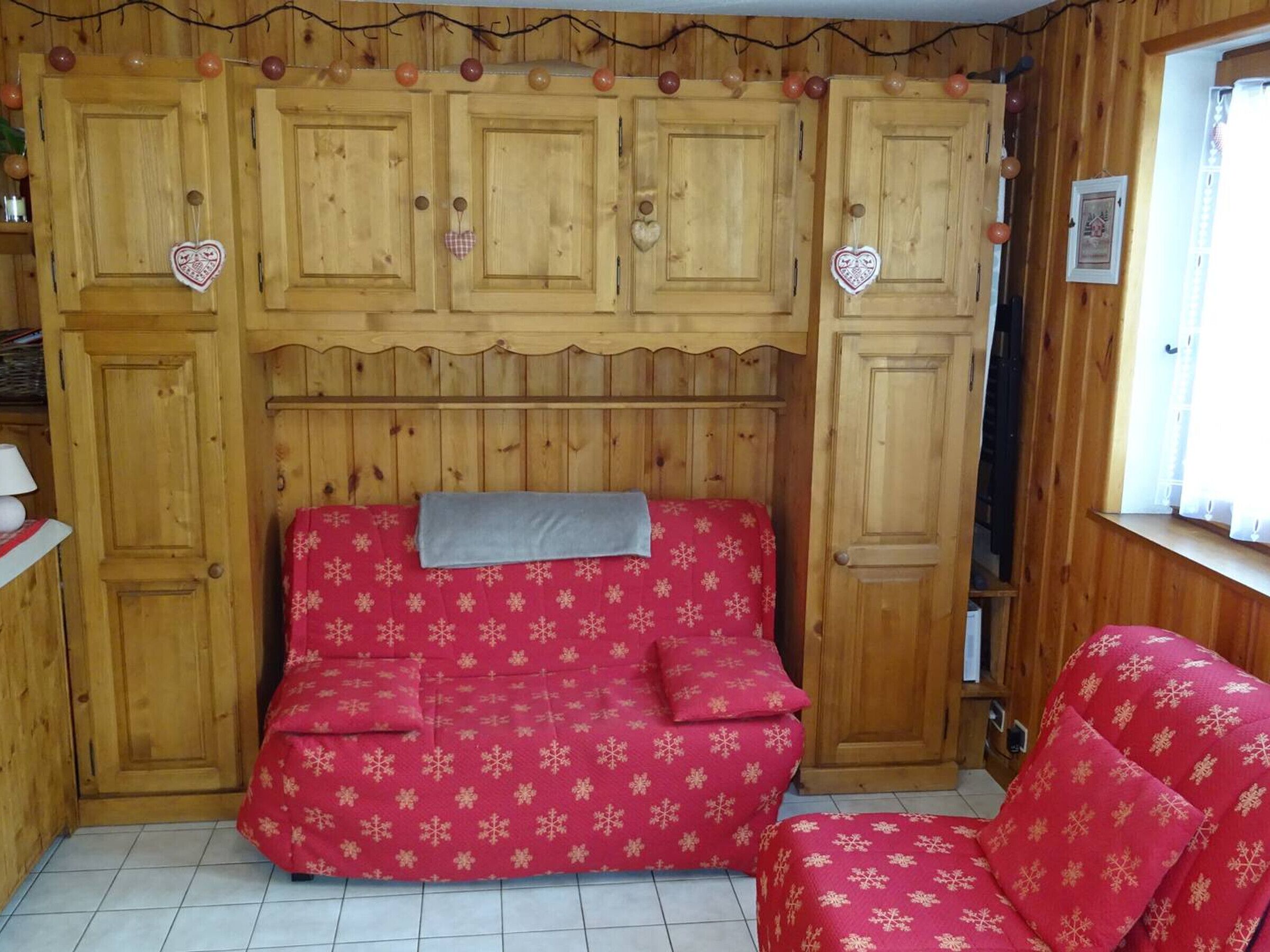 Una habitació acollidora amb un mur de fusta, un sofà vermell amb dibuixos de flocs de neu i una finestra amb cortines.