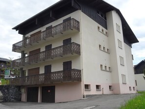 Un edificio de varios pisos con balcones, una pared de piedra y una zona de estacionamiento.